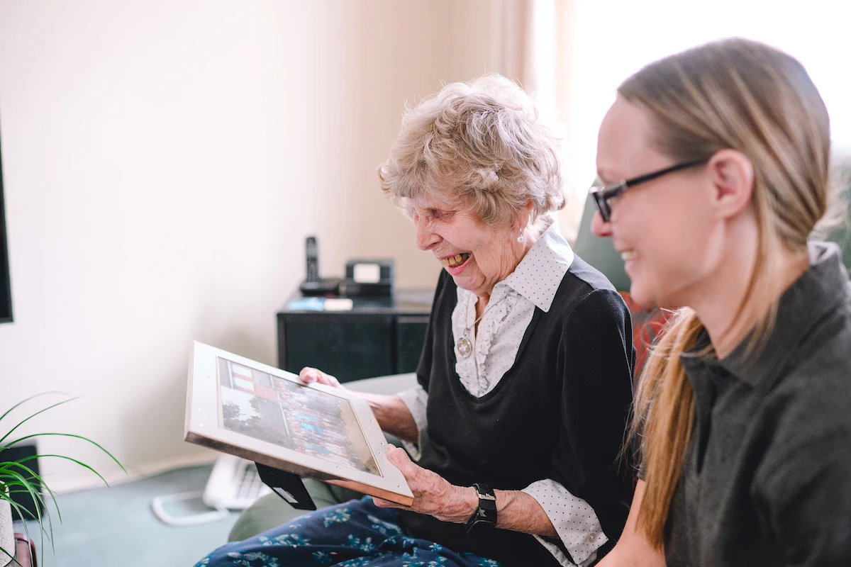 Elderly woman laughing while looking at photos with her home care assistant companion.
