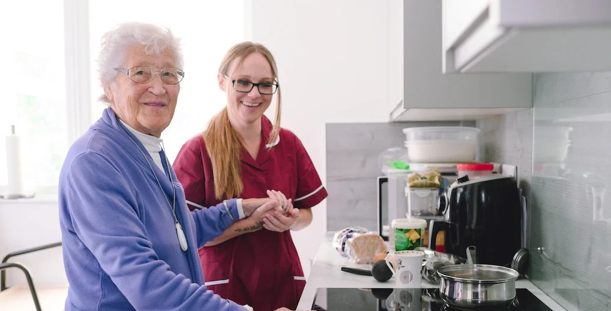 Home care assistant supporting an elderly woman with meal preparation in her kitchen.