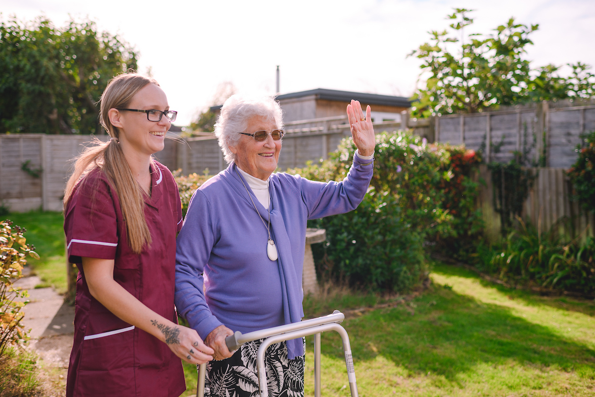 Home care assistant supporting an elderly woman using a walking frame in her Brighton and Hove garden.