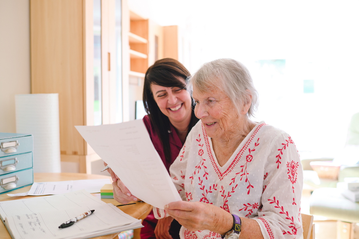 Nestwell home care assistant helping an elderly woman read paperwork at her home in Brighton.