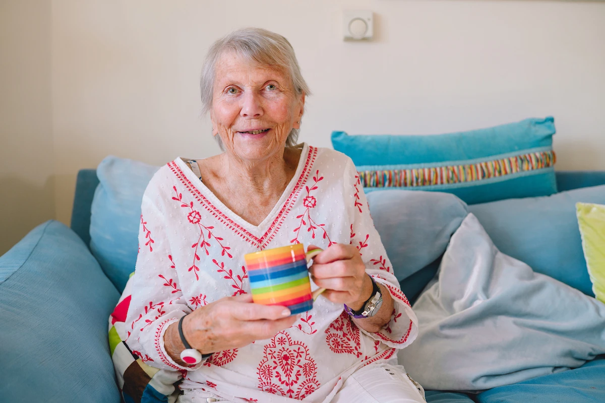 Smiling elderly woman holding a mug while relaxing on her sofa at home.